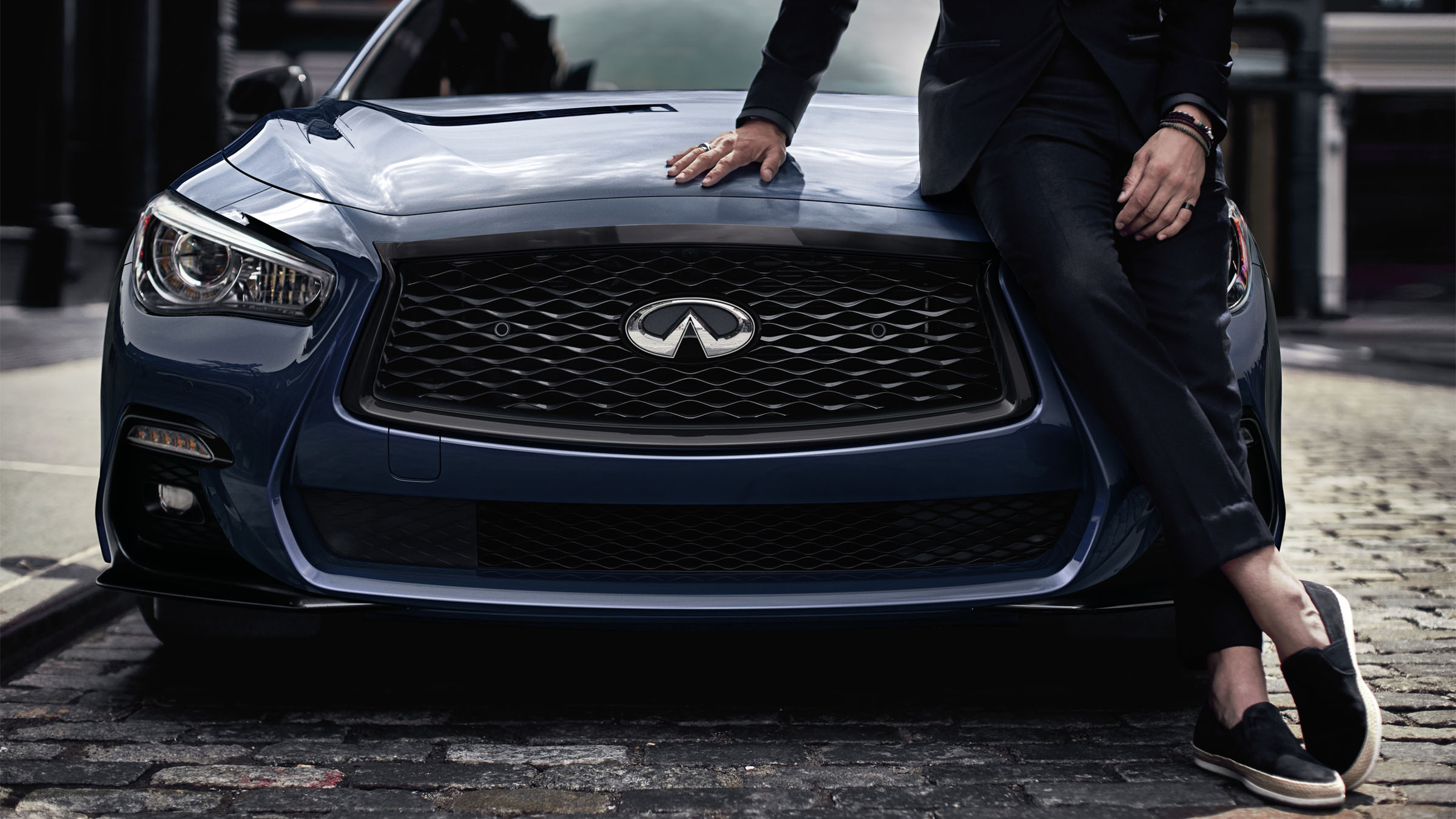 Person leaning on a blue 2022 INFINITI Q50.