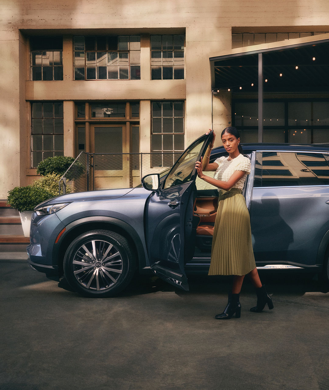 Driver getting out of the 2024 INFINITI QX60 3-row SUV in Moonbow blue parked on the road