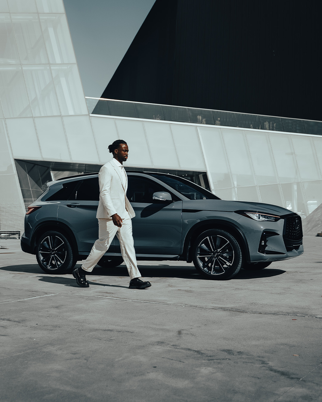 Driver in a white suit walking next to the 2024 INFINITI QX50 compact SUV in blue grey